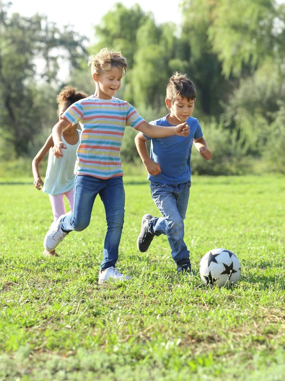 A group of children playing soccer in a grassy field during out-of-school hours