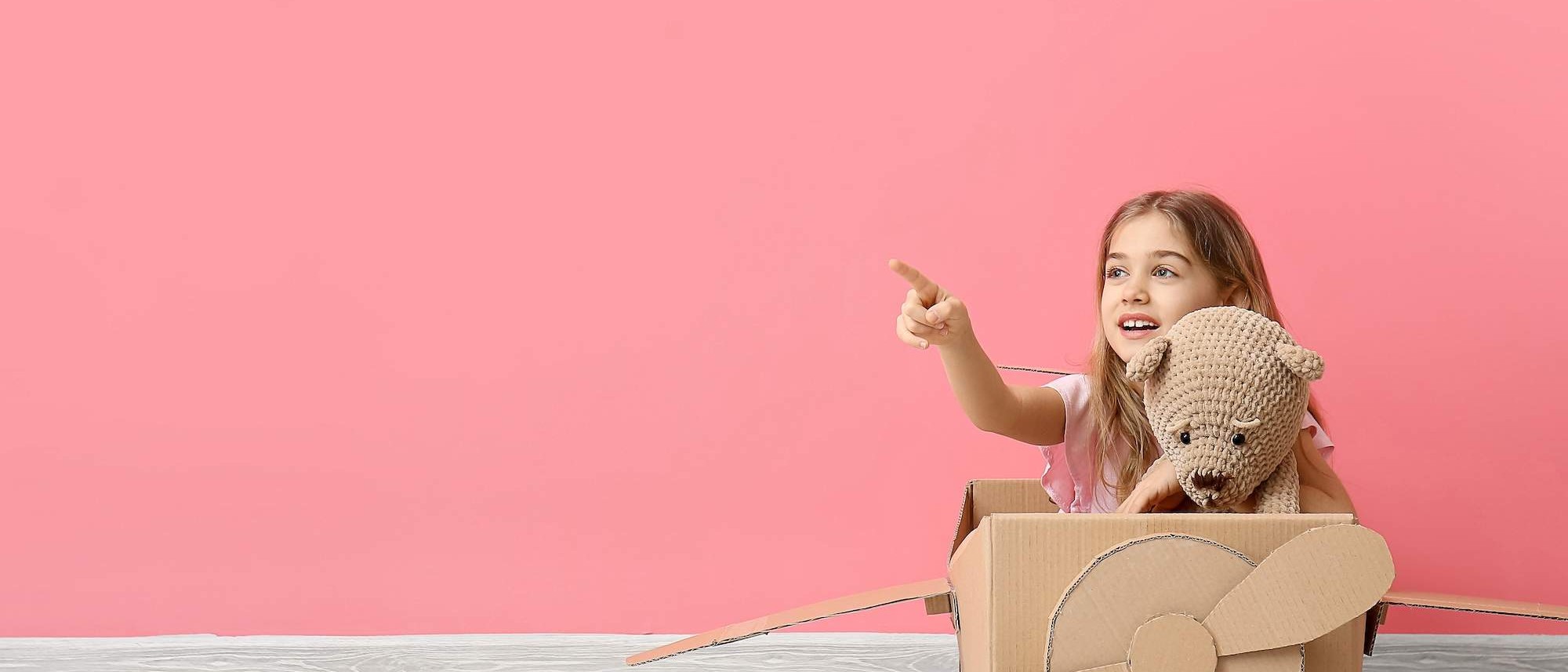 Girl in cardboard airplane pointing ahead during imaginative play at Calgary daycare
