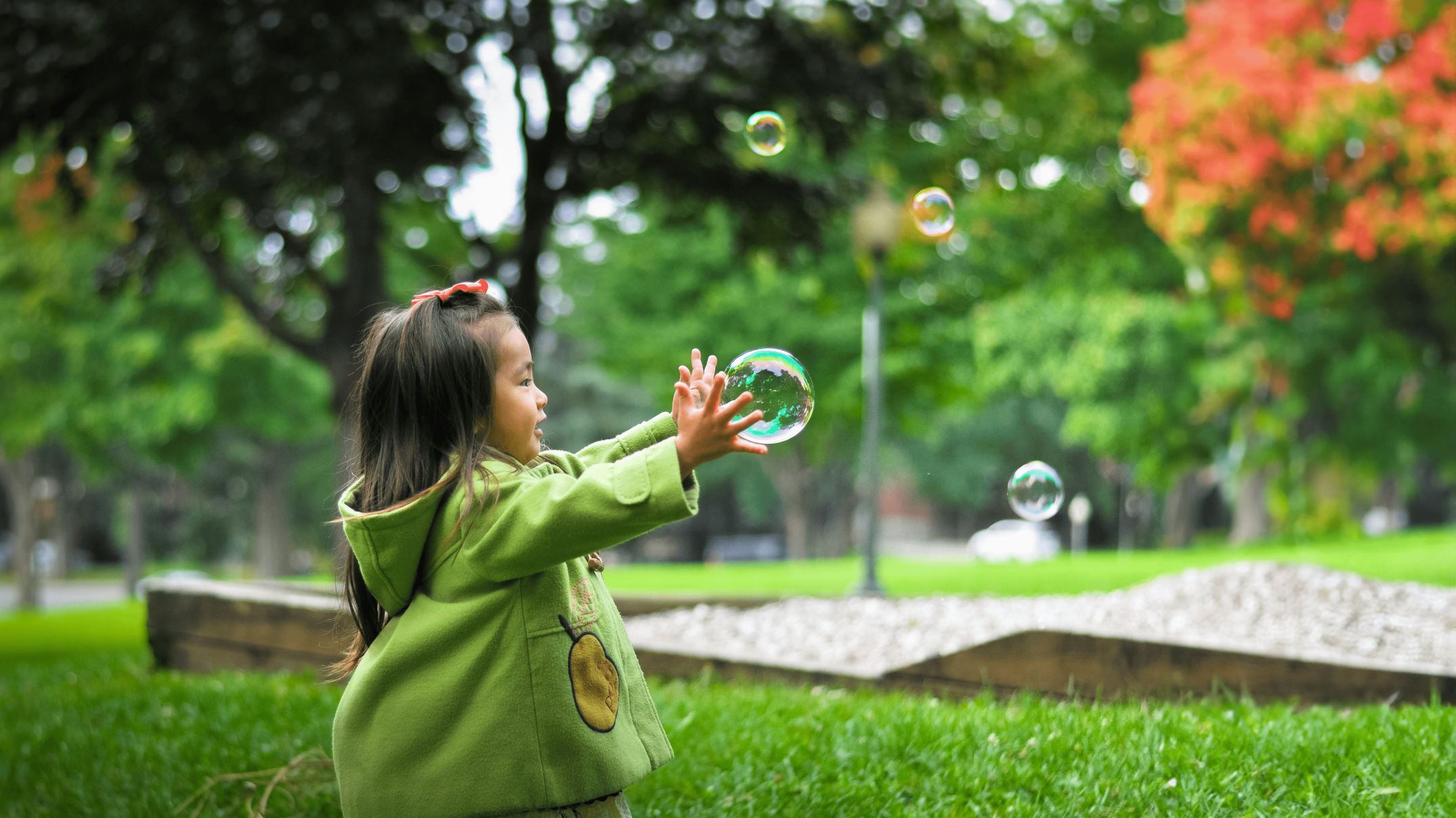 Young girl in a green hooded coat playing with bubbles on a playground at a Calgary childcare centre
