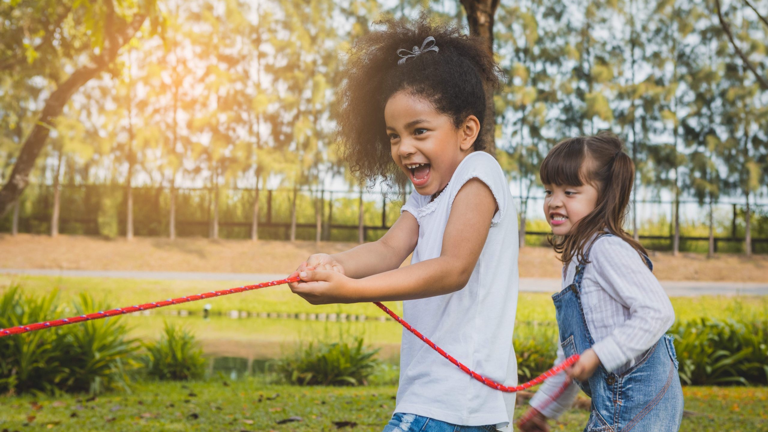 Two girls playing tug of war at Calgary daycare in outdoor field