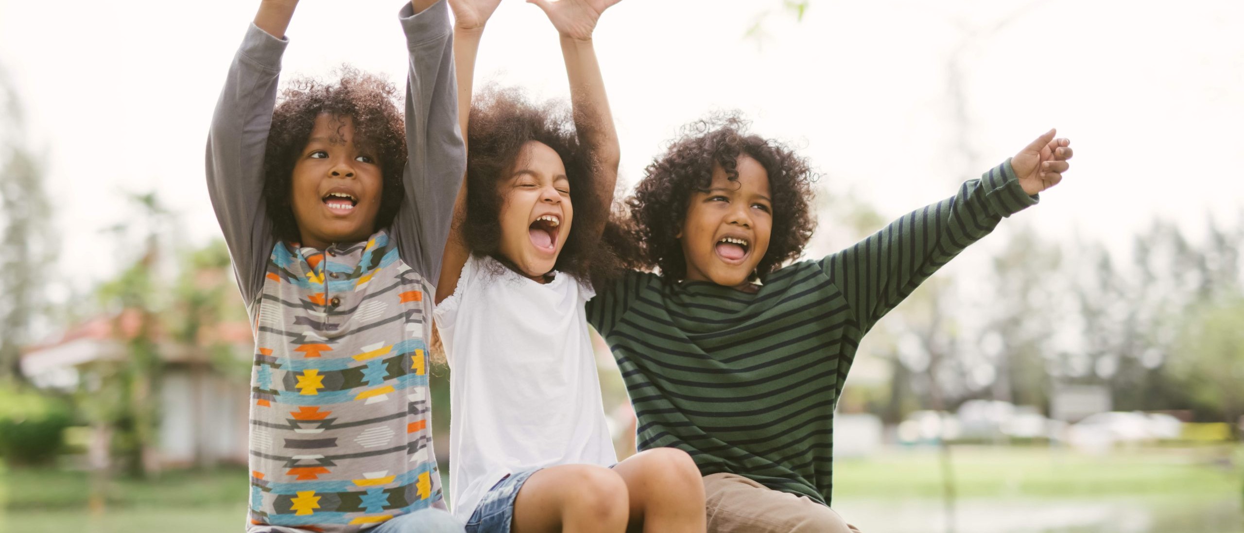 Three kids sitting on a bench outside cheering and waving arms