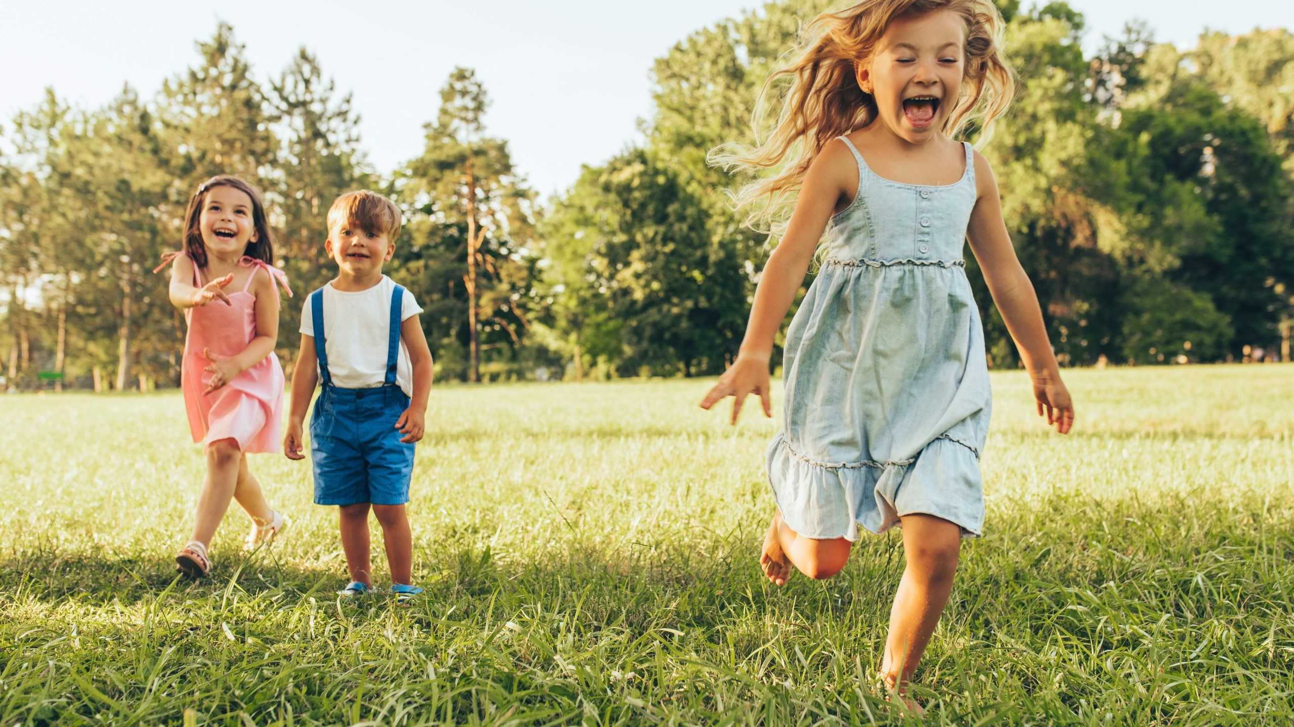 Three young children running and laughing in a sunny field near Calgary