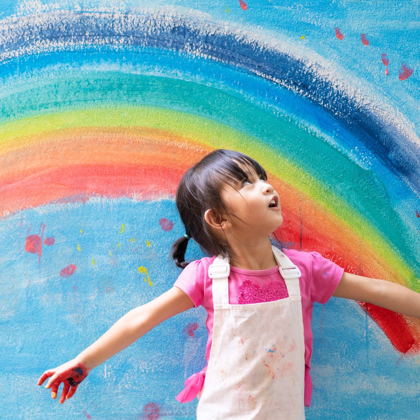 Child with painted hands standing in front of a rainbow mural at a Calgary childcare centre