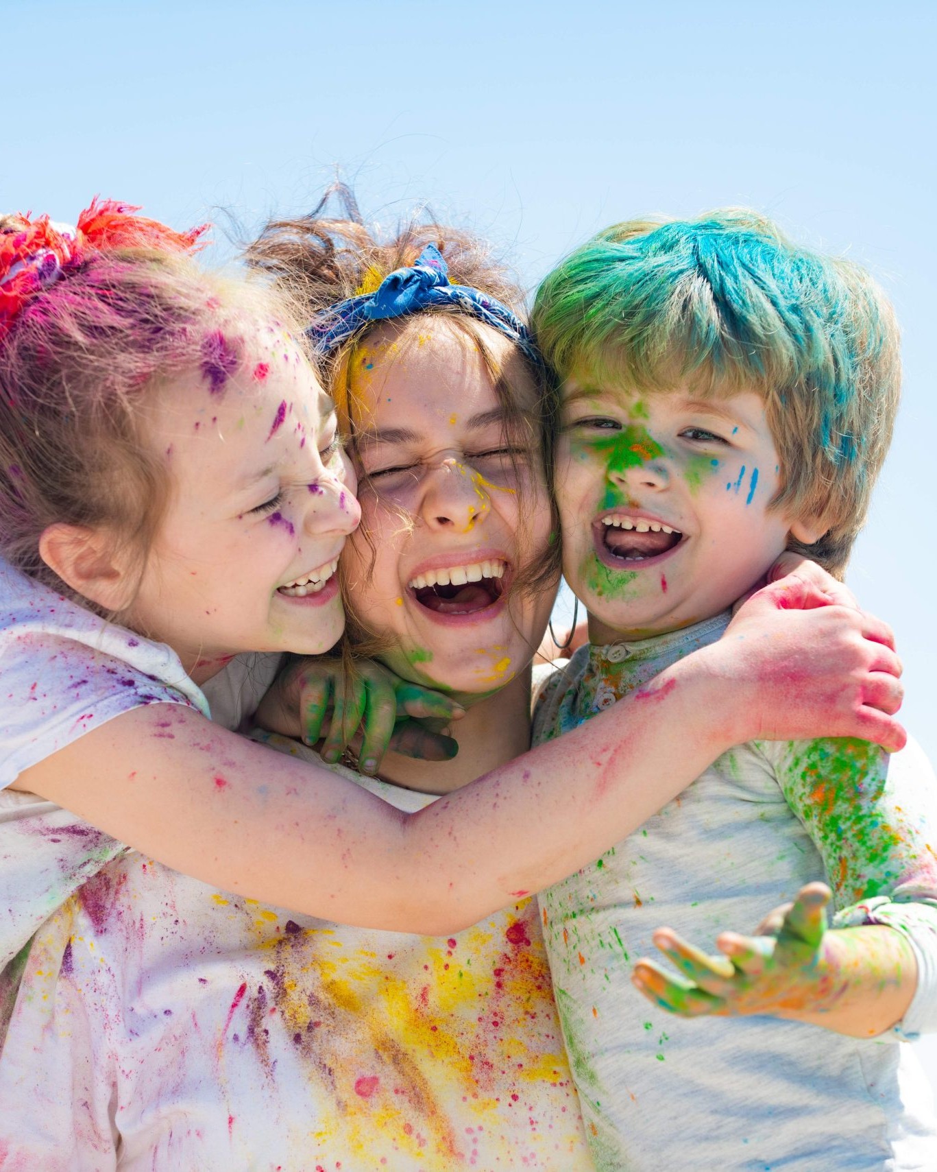 Group of three children laughing and hugging, covered in colorful paint at a Calgary childcare centre